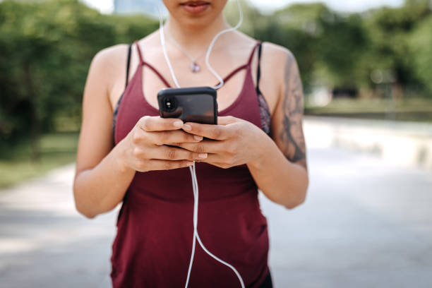istock Young Latin woman text messaging using smart phone at public park 1206461301