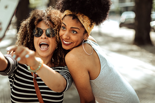 Two hipster female friends standing on the street, taking selfie and having good time