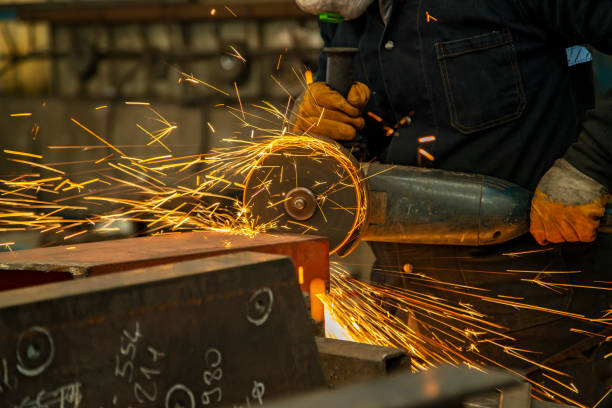 Worker man working with electric grinder tool on steel structure in factory.
