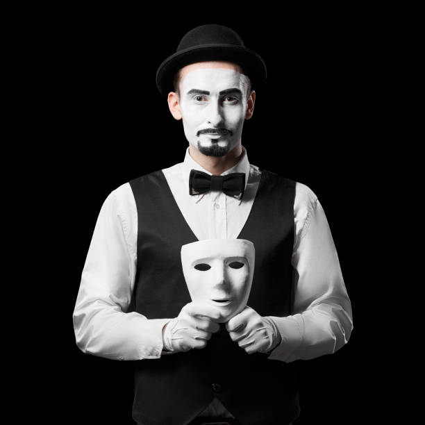 Mime artist holding white mask. Isolated on black background. Concept of people masks and lies stock photo