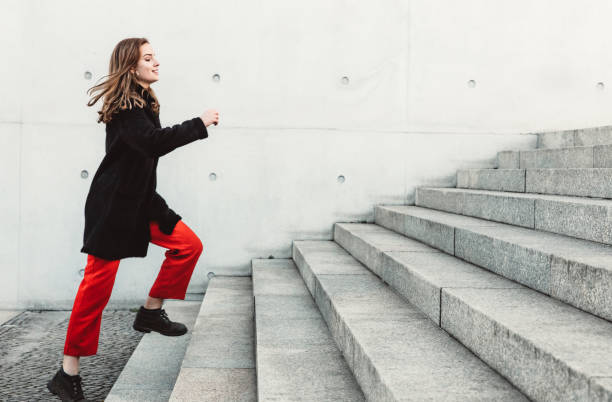 Woman climbing up the stairs Young woman running up the steps outdoors. Woman in warm clothes climbing up the stairs. moving up stock pictures, royalty-free photos & images