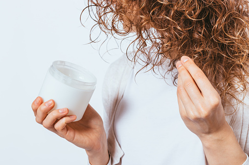 Female's hands apply cosmetic coconut oil on her curly hair tips, close-up.