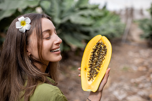Portrait of a young woman with sliced papaya fruit on the plantation. Concept of vegetarianism, healthy eating of fresh fruits, skin care and wellbeing