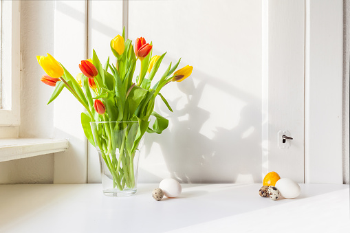 red and yellow tulips in vase on the windowsill bright, country style, in sunlight, bouquet for Easter decoration against an open background with copy space