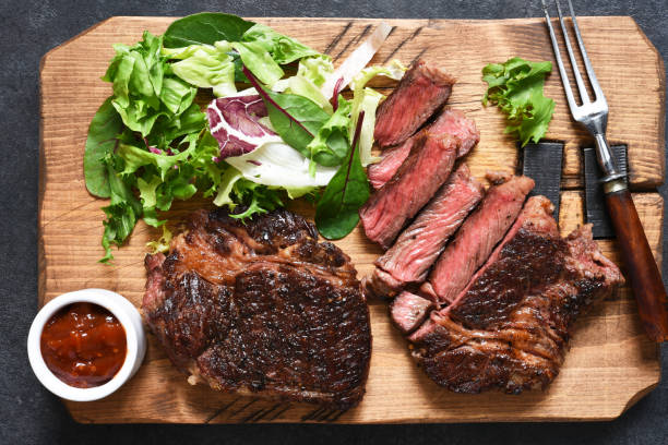 bife de carne de mármore grelhado com salada em uma tábua de madeira na mesa da cozinha. com espaço de cópia o texto. - sirloin steak top sirloin onion food state - fotografias e filmes do acervo