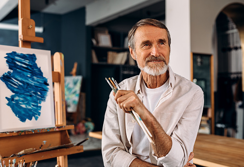 Portrait of a smiling mature painter sitting in his studio and looking away