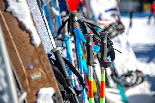 An assortment of various skis, snowboards and ski poles racked at the base of a Colorado ski resort outside of the the ski lodge.