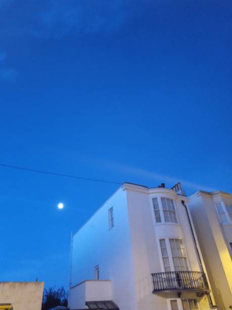 istock Moon in blue dawn sky with street’s houses UK 1206522936