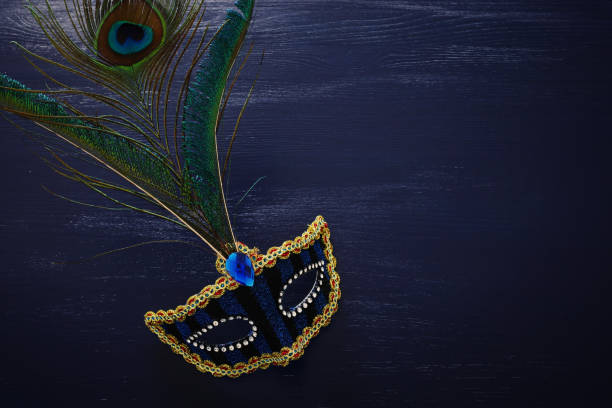 暗い木製の背景の上に美しい孔雀の羽とエレガントで繊細な青いベネチアンマスクの写真 - carnival mardi gras mask peacock ストックフォトと画像