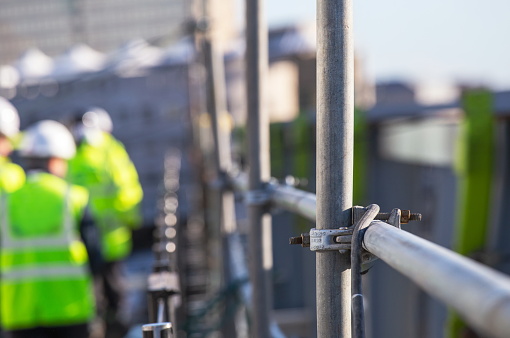 Silhouette Construction workers on a scaffold - Extensive scaffolding providing platforms for work in progress - Men walking on roof surrounded by scaffold - Focus on scaffolding frame - Blue filter