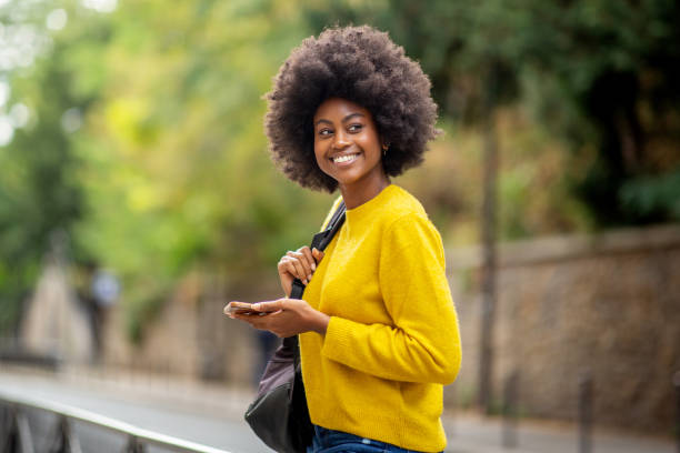 istock smiling young black woman holding mobile phone and bag 1206532490