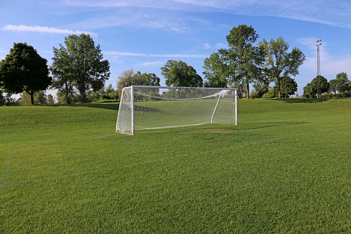 A view of a net on a vacant soccer pitch in morning light.