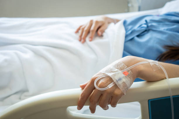 mujer paciente que duerme con recibir líquido intravenoso directamente en una vena mientras su mano toca los rieles de la cama en la cama del hospital. - solución salina fotografías e imágenes de stock