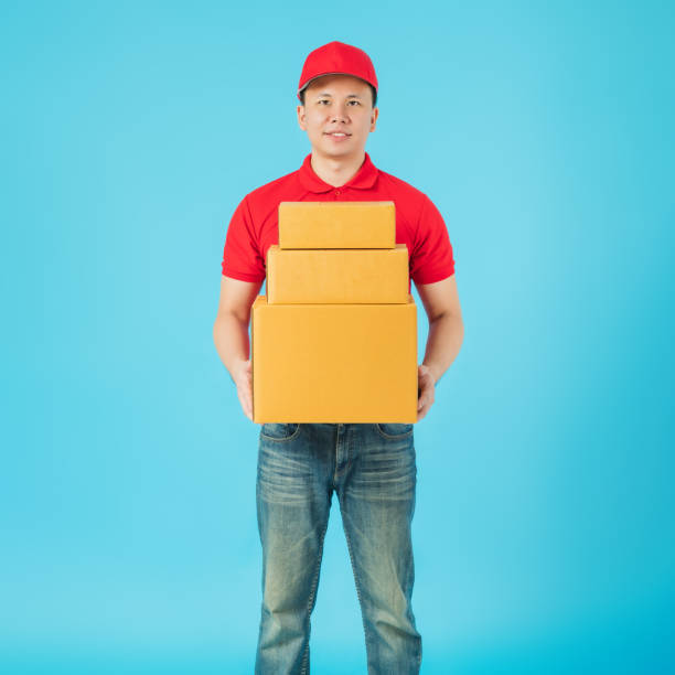 istock Asian happy delivery man carrying paper parcel boxes isolated on blue colour background.Concept of Postal delivery service. 1206562268