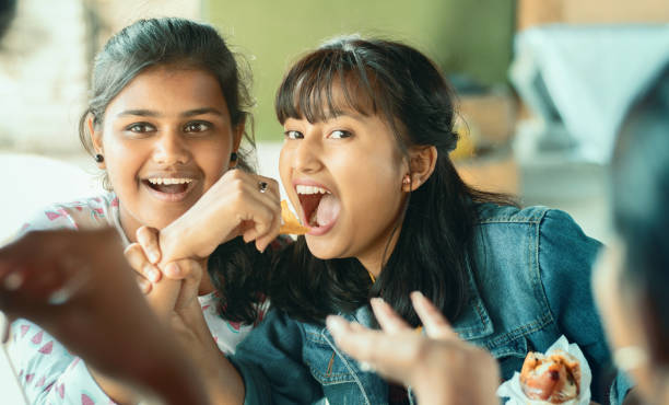 Teenager trying to take or grab food from friend - young girl playfully fighting for snacks with her friend - concept of friends having fun while having food at college restaurant. Teenager trying to take or grab food from friend - young girl playfully fighting for snacks with her friend - concept of friends having fun while having food at college restaurant family eating potato chips stock pictures, royalty-free photos & images