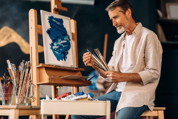 istock Mature painter holding a bunch of paint brushes sitting in studio 1206574289