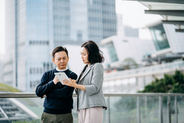 istock Two business persons using digital tablet and discussing on a business project outdoors against city scene in front of modern office buildings 1206575185