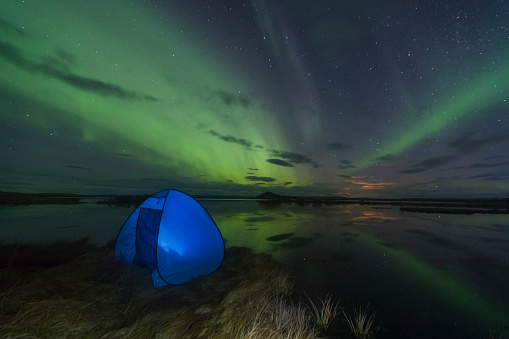 Aurora Borealis (Northern lights) above a camping tent in the Icelandic wilderness near lake