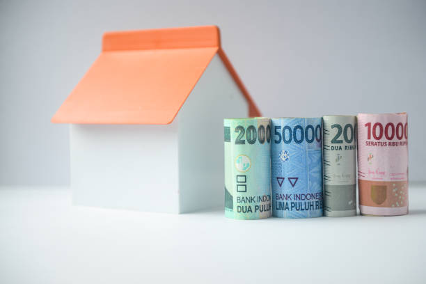 istock Indonesian Rupiah rolled banknotes and house model on white background 1206576141