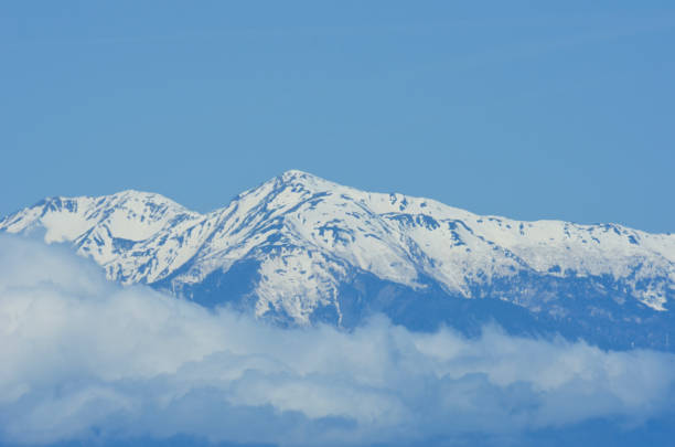 istock A snow-topped mountain range rises above white clouds into a blue sky. 1206579924