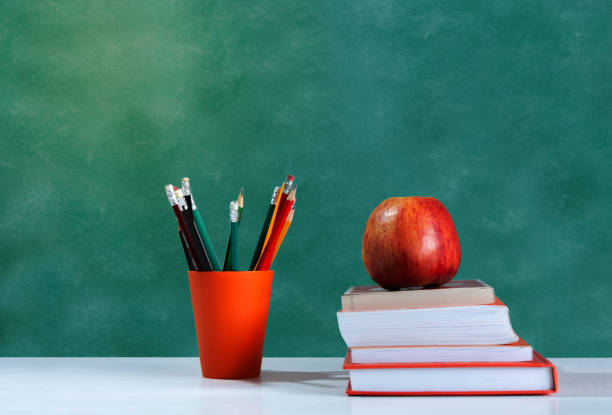 istock Back to school, orange pencil holder, stack of books on white table with red apple, empty school board background, education concept 1206585853