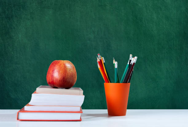 istock Back to school, orange pencil holder, stack of books on white table with red apple, empty school board background, education concept 1206585854