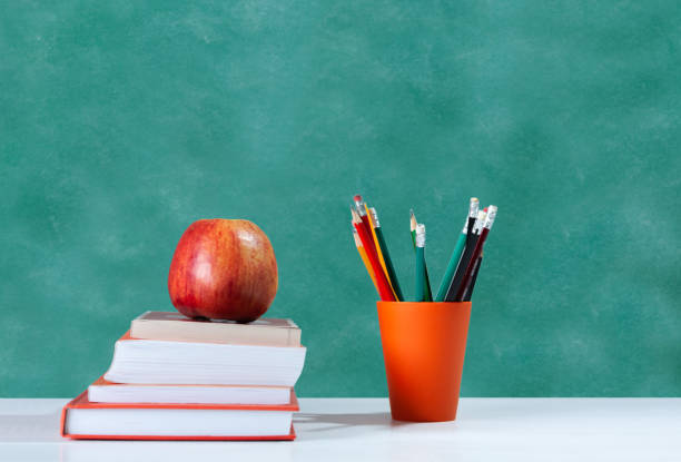 istock Back to school, orange pencil holder, stack of books on white table with red apple, empty school board background, education concept 1206585855