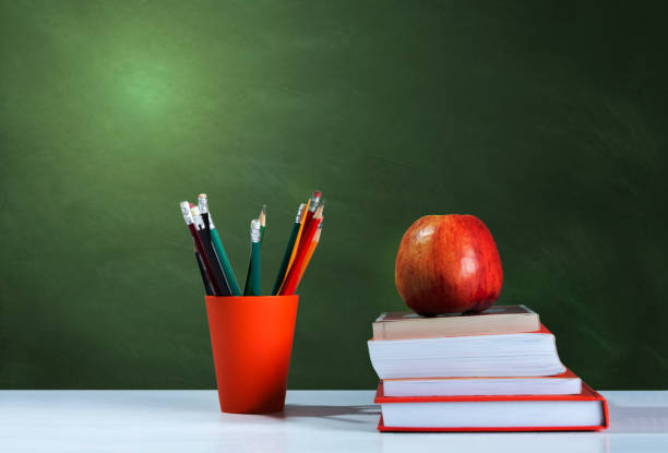 istock Back to school, orange pencil holder, stack of books on white table with red apple, empty school board background, education concept 1206585865