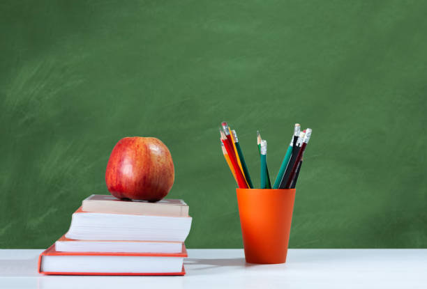 istock Back to school, orange pencil holder, stack of books on white table with red apple, empty school board background, education concept 1206585866