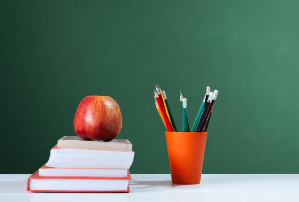 istock Back to school, orange pencil holder, stack of books on white table with red apple, empty school board background, education concept 1206585867