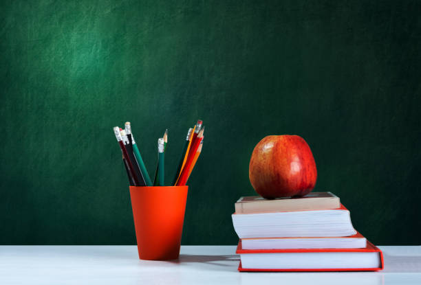 istock Back to school, orange pencil holder, stack of books on white table with red apple, empty school board background, education concept 1206585868