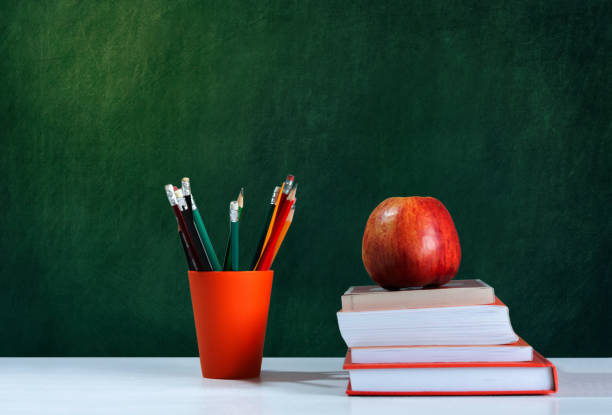 istock Back to school, orange pencil holder, stack of books on white table with red apple, empty school board background, education concept 1206585888