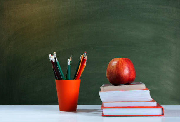 istock Back to school, orange pencil holder, stack of books on white table with red apple, empty school board background, education concept 1206585891