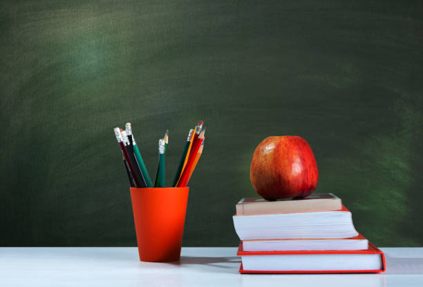 istock Back to school, orange pencil holder, stack of books on white table with red apple, empty school board background, education concept 1206585903