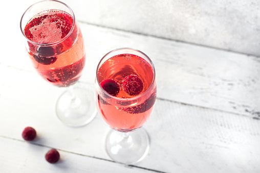 Kir Royal Champagne Cocktail on white, copy space. Flute glasses with berry sparkling champagne drink for celebrating or chilling.