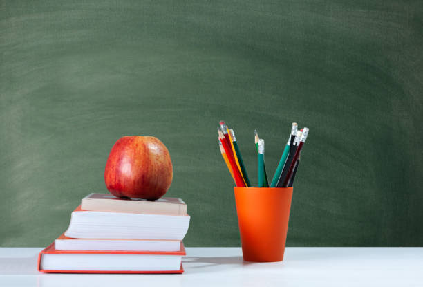 istock Back to school, orange pencil holder, stack of books on white table with red apple, empty school board background, education concept 1206586806