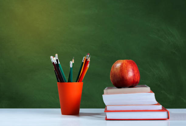 istock Back to school, orange pencil holder, stack of books on white table with red apple, empty school board background, education concept 1206586823