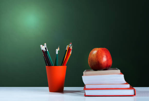 istock Back to school, orange pencil holder, stack of books on white table with red apple, empty school board background, education concept 1206586829