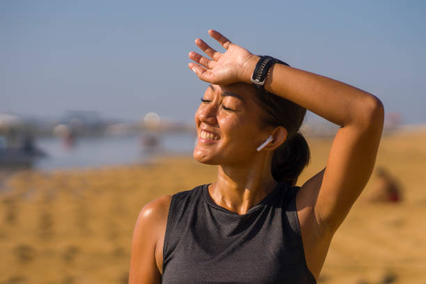 portrait of young attractive and sweaty happy Asian Indonesian woman in her 40s smiling satisfied after hard beach running workout in sports training and healthy lifestyle concept stock photo