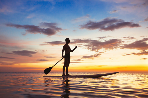 paddle standing board, beach leisure activity, beautiful silhouette of man at sunset