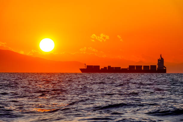 Sea near the coast. Bright orange sunset. Big sun and silhouette of a container ship