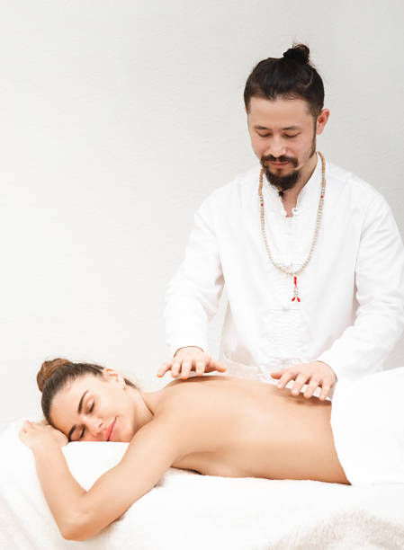 docteur de médecine orientale traditionnelle faisant le massage énergique de non contact à une belle femme dans un salon de spa. le corps est purifié d’énergie négative. massage reiki - reiki alternative therapy massaging women photos et images de collection