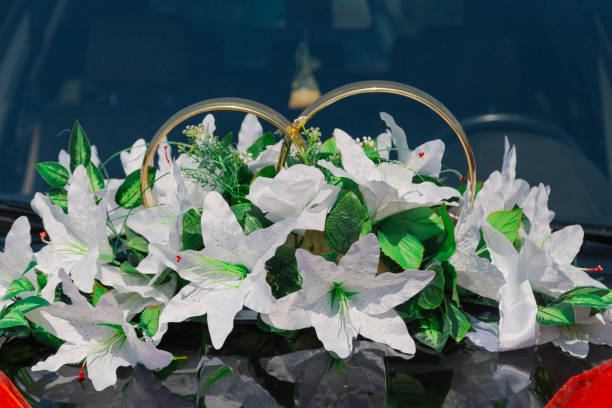Heidelberg, Germany- May 21, 2016-A large bouquet of flowers including several peonies are tied to the hood of a white BMW as a decoration with ribbons with a joined ring motif in celebration of a afternoon wedding.