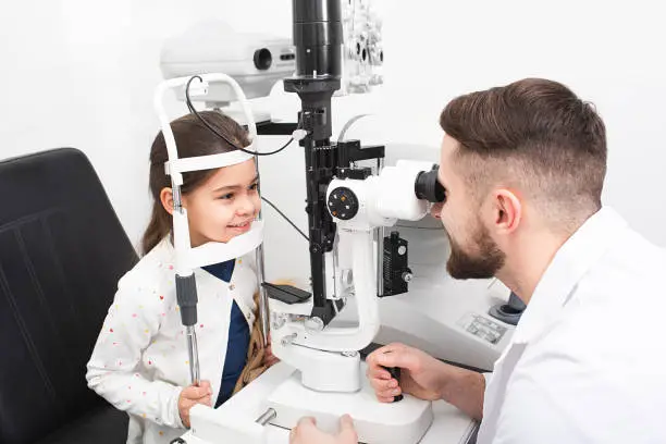 Optometrist doctor using a binocular slit-lamp examines the eye of a patient's girl. Children must be tested by an ophthalmologist