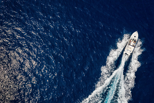 Aerial view of a speedboat traveling over blue sea leaving a trail of white waves and bubbles behind with copy space