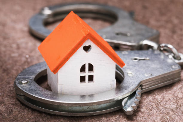 Small toy house and handcuffs. Real Estate Fraud Concept stock photo