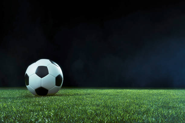 Traditional football on an illuminated sports field at night Traditional football on an illuminated empty sports field at night backlit by bright spotlights in a low angle view with shadow, mist and copy space international team soccer photos stock pictures, royalty-free photos & images