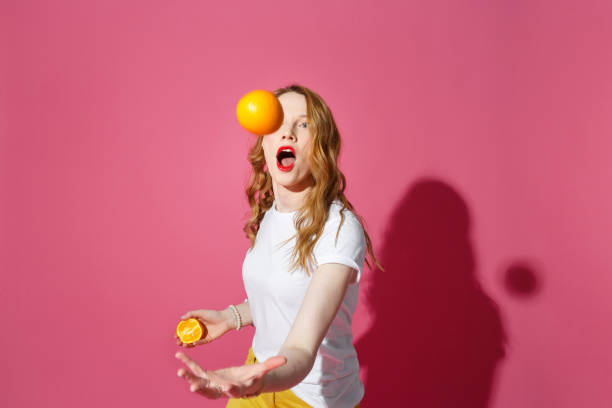 oranje vruchten, gezond eten, ware emoties - een jonge blonde vrouw die sinaasappels op roze achtergrond jongleert - jongleren stockfoto's en -beelden