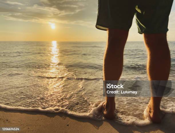 Man In Shorts Meets Beautiful Sunset Sunrisesea Wave With Foam Touches Legs Stock Photo - Download Image Now