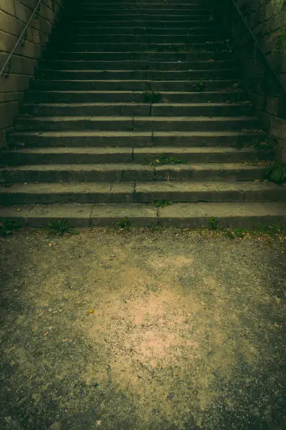 Photo of Wide staircase in a park made of natural stone with a handrail made of rusted steel in the dim light with a creepy and scary aura like in a thriller